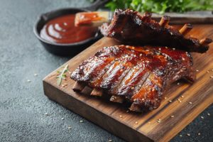Glazed BBQ ribs on a wooden cutting board next to a small black skillet of BBQ sauce at a restaurant in Springfield, IL.