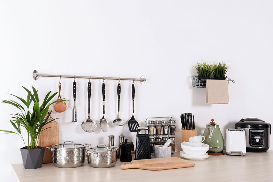 A set of clean cookware, dishes, utensils, and appliances on a kitchen counter in front of a white wall in Springfield, IL.