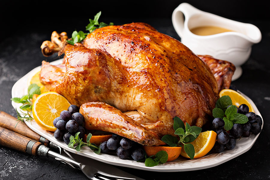 A fully cooked, golden-brown turkey on a plate surrounded by oranges, blueberries, and a gravy boat, prepared for Thanksgiving in Springfield, IL.